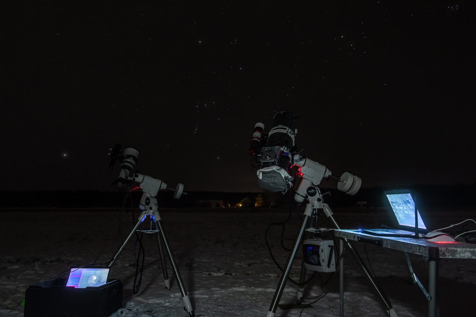 Kuvassa Jannen laitteiden vieressä Heikki Ahon astrokuvauskalusto. Kamerat seisovat jalustoilla pimeällä lumisella pellolla.